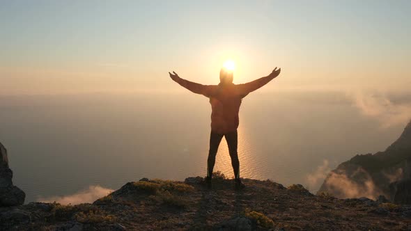 Silhuette of Young Man Arms Outstretched Observing Beautiful Dramatic Colorful Sunset Above a Sea