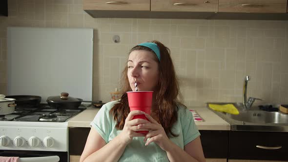 Woman Sitting in the Kitchen at Home and Drinking Soda From a Red Glass