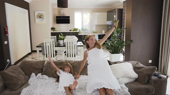 Attractive Two Girls Fun Falling and Lies on the Sofa Spreading their Arms in the Living Room