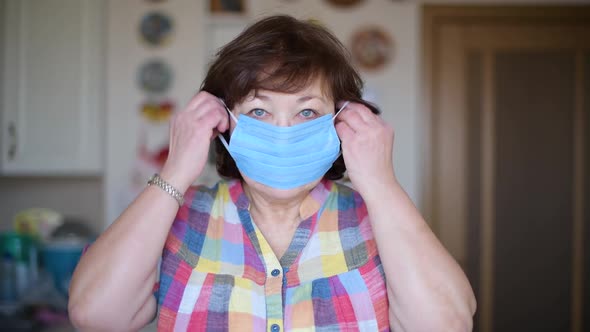 An aged woman puts on a protective medical mask and looks at the camera