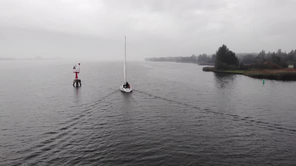 Dutch sailing vessel navigating on a fairway between buoy while the trees on the shore are in autumn