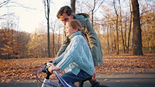 Young Dad Teaching Daughter to Ride a Bike Holding Seat and Handlebar By His Hands