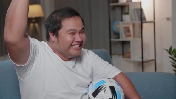 Excited Asian Fat Man Watches Tv While Sitting On A Couch At Home