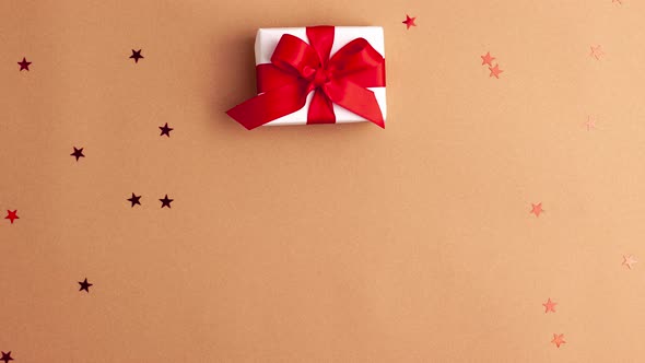 Human hands with red sleeves putting a white paper gifts with a red satin ribbon bow on brown back