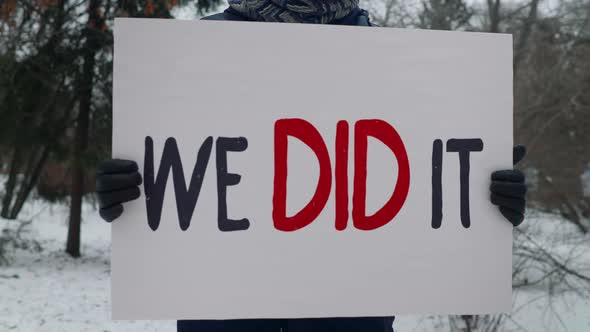 Man wears winter clothes and holds a sign with a phrase saying we did it