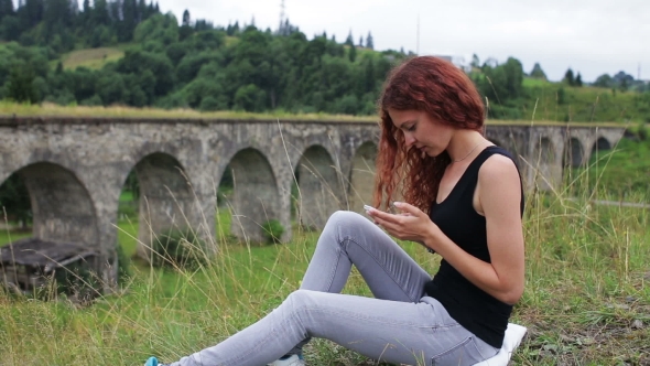 The Girl Writes Sms Sitting Near The Old Viaduct In The Mountains