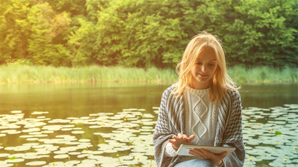 Beautiful Girl Using Tablet PC Sitting Near Lake in City Park 1 on Sunset 