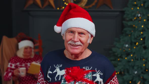 Senior Grandfather in Festive Sweater Presenting Christmas Gift Box Smiling Looking at Camera