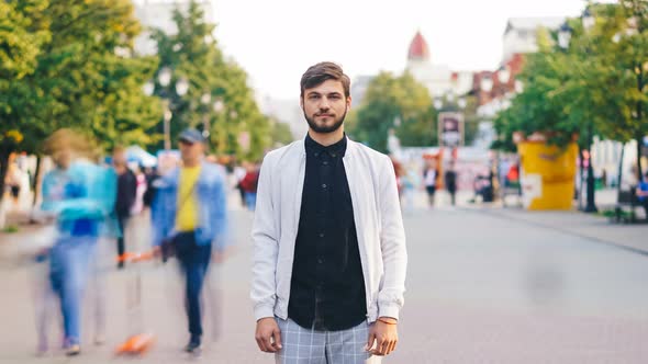 Time-lapse Portrait of Serious Young Man Looking at Camera Standing in Center of Busy Pedestrian