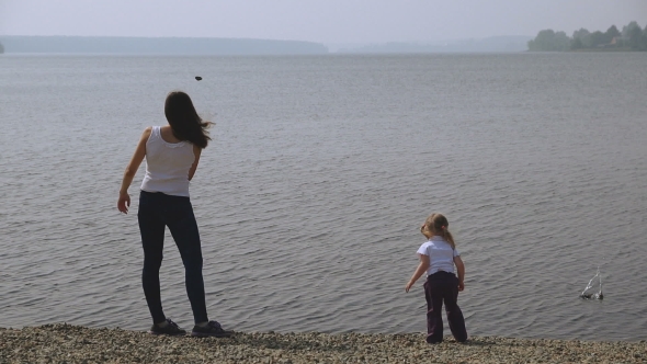 Mother And Daughter Throwing Rocks Into The Pond.