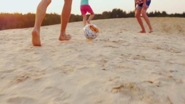 Family Playing Football. In The Frame Of The Man Legs Hit The Ball The Ball On The Sand