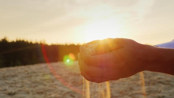 Sand Pours From The Man's Hands At Sunset. Concept: The Transience Of Time, Changes Lifetime
