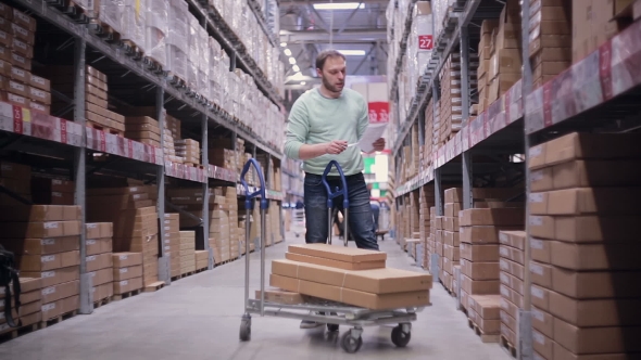 A Man With a Trolley In a Warehouse. He Is Checking His List And Taking Necessary Boxes
