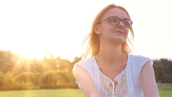 Happy Beautiful Young Woman Sitting on the Grass in City Park and Smiling at Sunset 2