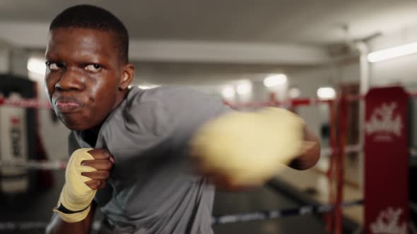 Young Confident African Male Boxer Wearing Boxing Bandage on Hands Punching at Camera During Workout