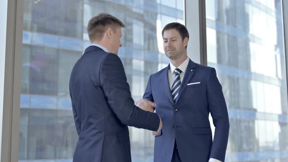 Two Middle Aged Businessmen Shaking Hand and Sharing Money Against Office Window