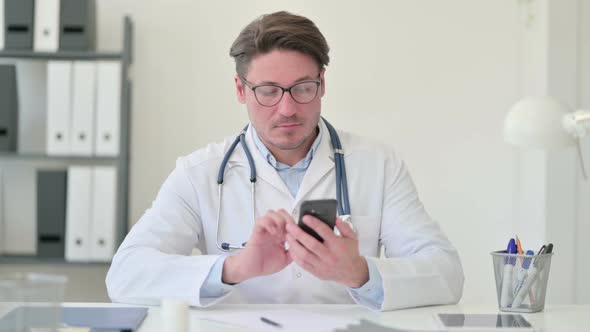 Middle Aged Male Doctor Using Smartphone in Office