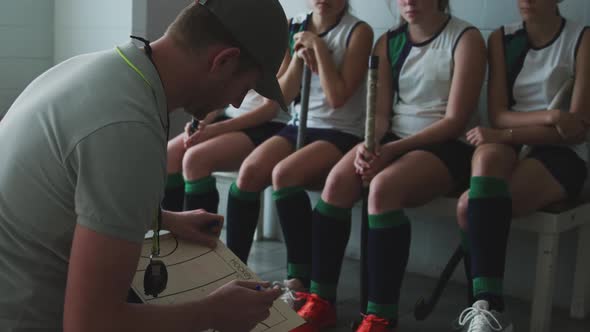 Hockey coach explaining game plan with female players in locker room