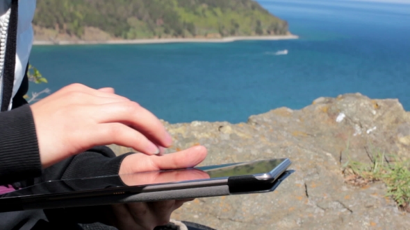 Female Sitting On The Shore Of Lake Baikal On a Rock And Using a Tablet