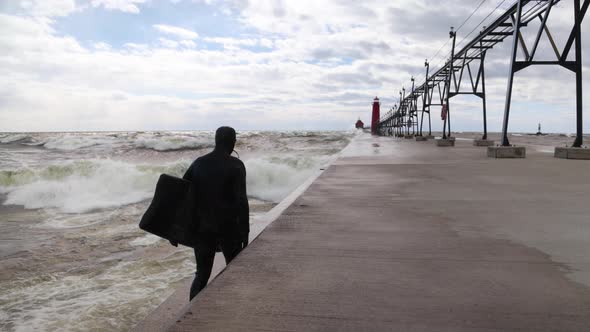 Walking behind surfer on Grand Haven, Michigan pier on Lake Michigan in slow motion.