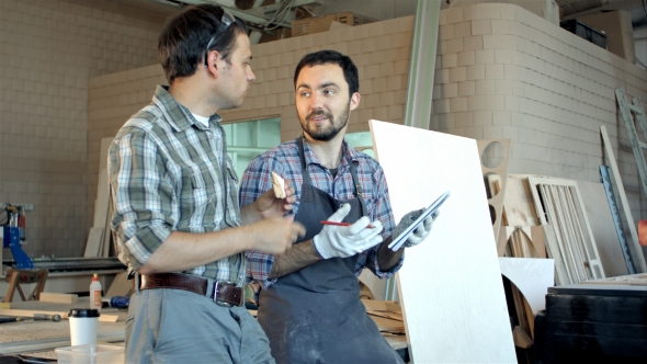 Two Carpenters Discussing Ideas One Of Them Eating And Another Is Writing In Notebook At Workshop.