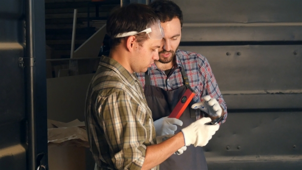 Two Carpenters Discussing Something And Watching Something On The Tablet In Workshop.