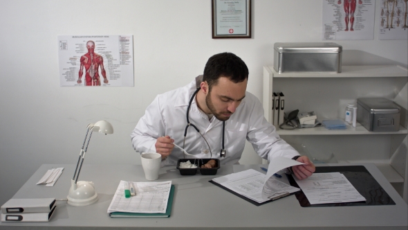 Doctor Woking Whith Documents During Having a Lunch At His Office. Employee Eating From Lunchbox