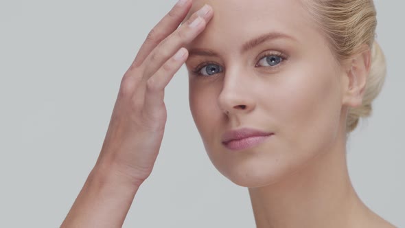 Studio portrait of young, beautiful and natural blond woman applying skin care cream. F