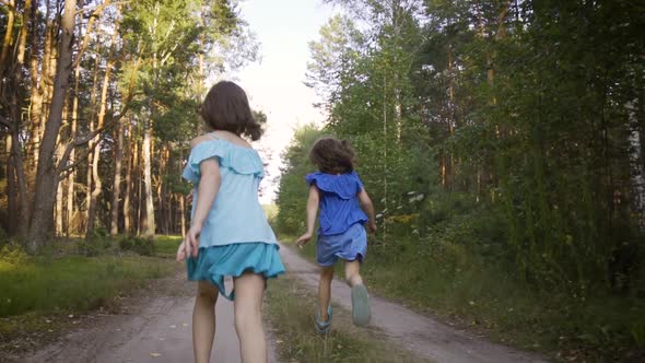 Two Cute Girls Are Running Along the Forest Road and Talking
