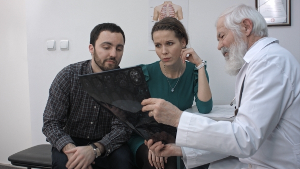 Male Senior Doctor Showing a Couple a X-ray In a Office.