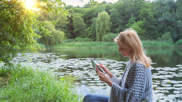 Beautiful Girl Using Tablet PC Sitting Near Lake in City Park 3
