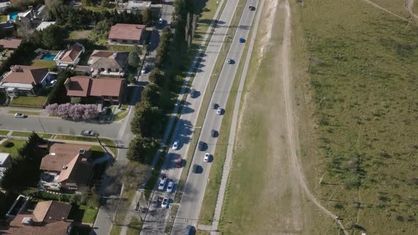 Aerial Drone shot of highway with cars going through and suburbs on side, tilting down