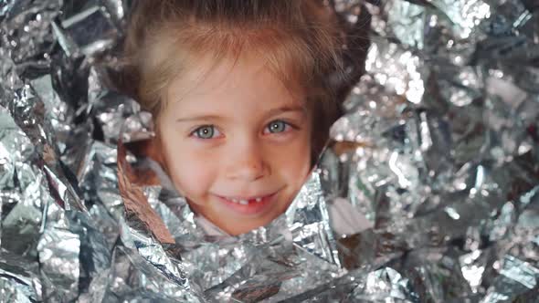 Little Girl Having Fun on Her Birthday Lies on the Floor on Shiny Confetti Silver Metaphan Close Up