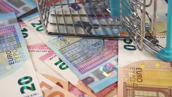 Medical masks fall on Euro bills with a mini shopping cart.