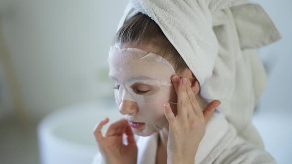 Close Up of a Young Domestic Woman Apply Tissue Face Mask for Skin Care Un the Bathroom