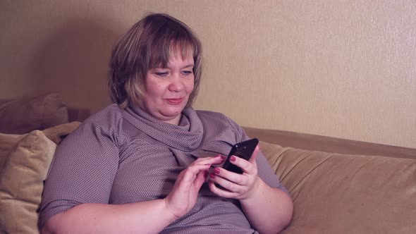 A Female Client on the Couch Holding a Smartphone in Her Hand is Making