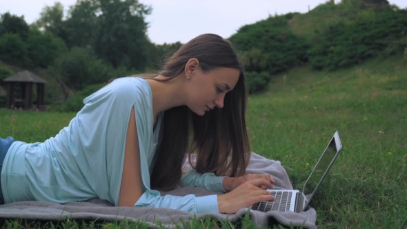 A Young Woman Lies On Lawn And Gaining a Message On The Computer. Laughing, Rejoicing.