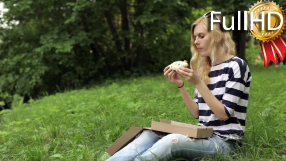 Girl Eating a Pizza Sitting on the Meadow