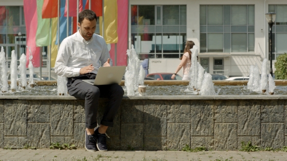 Business Man With Laptop Outside On a Bench Next To Fountain Working