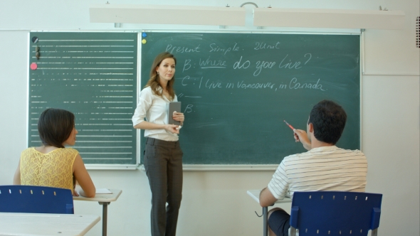 Young Female Teacher Writing On Chalkboard In Class