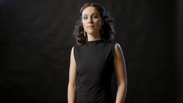 Beautiful Brunette With Wavy Hair Dressed In Black Dress, Crossing Her Arms, Looking At Camera