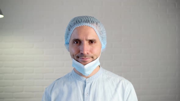 A tired male doctor removes his protective mask