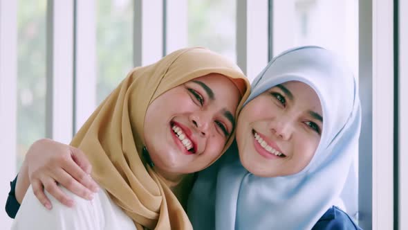 Close up of two young Muslim women wearing hijabs, hugging and smiling