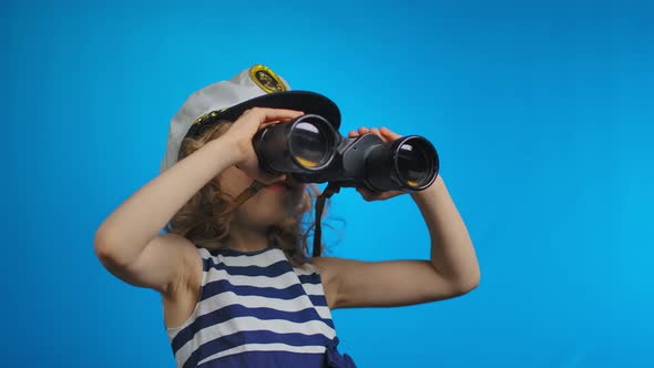 Little Blond Girl in Sailor Hat is Looking at the Sky Through the Binoculars