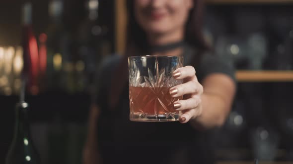 Attractive bartender holding mixed drink in crystal lowball glass, close.