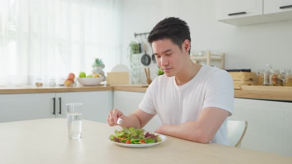 Portrait of Asian male look at camera while eat green salad in kitchen.