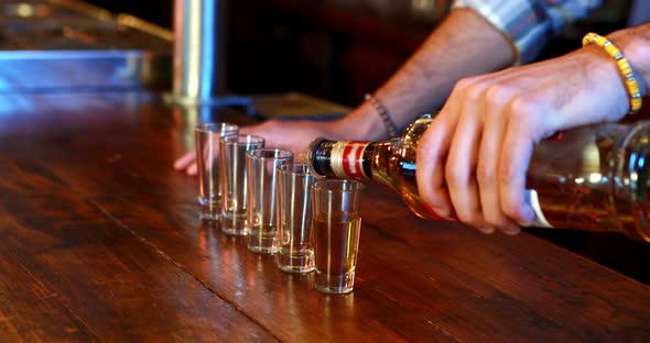 Barman pouring tequila in shot glass at bar counter