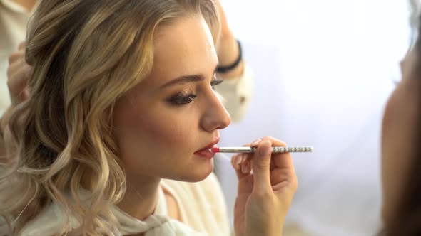 Side view of professional make-up artist applying makeup lips of young woman.