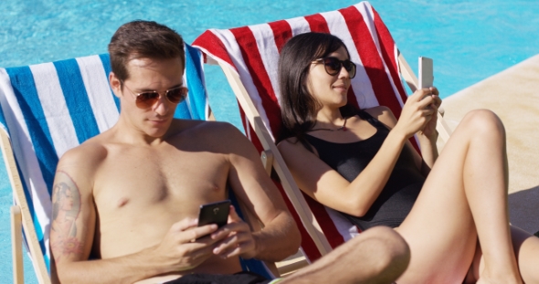 Young Couple Using Phones At The Swimming Pool