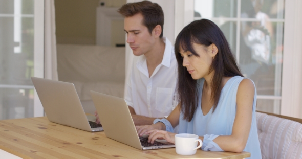 Calm Young Couple Sitting At Table Using Laptop